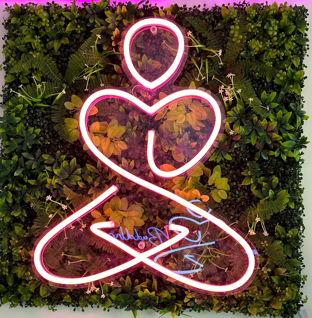 Pink neon Canna Buddha logo on a living plant wall